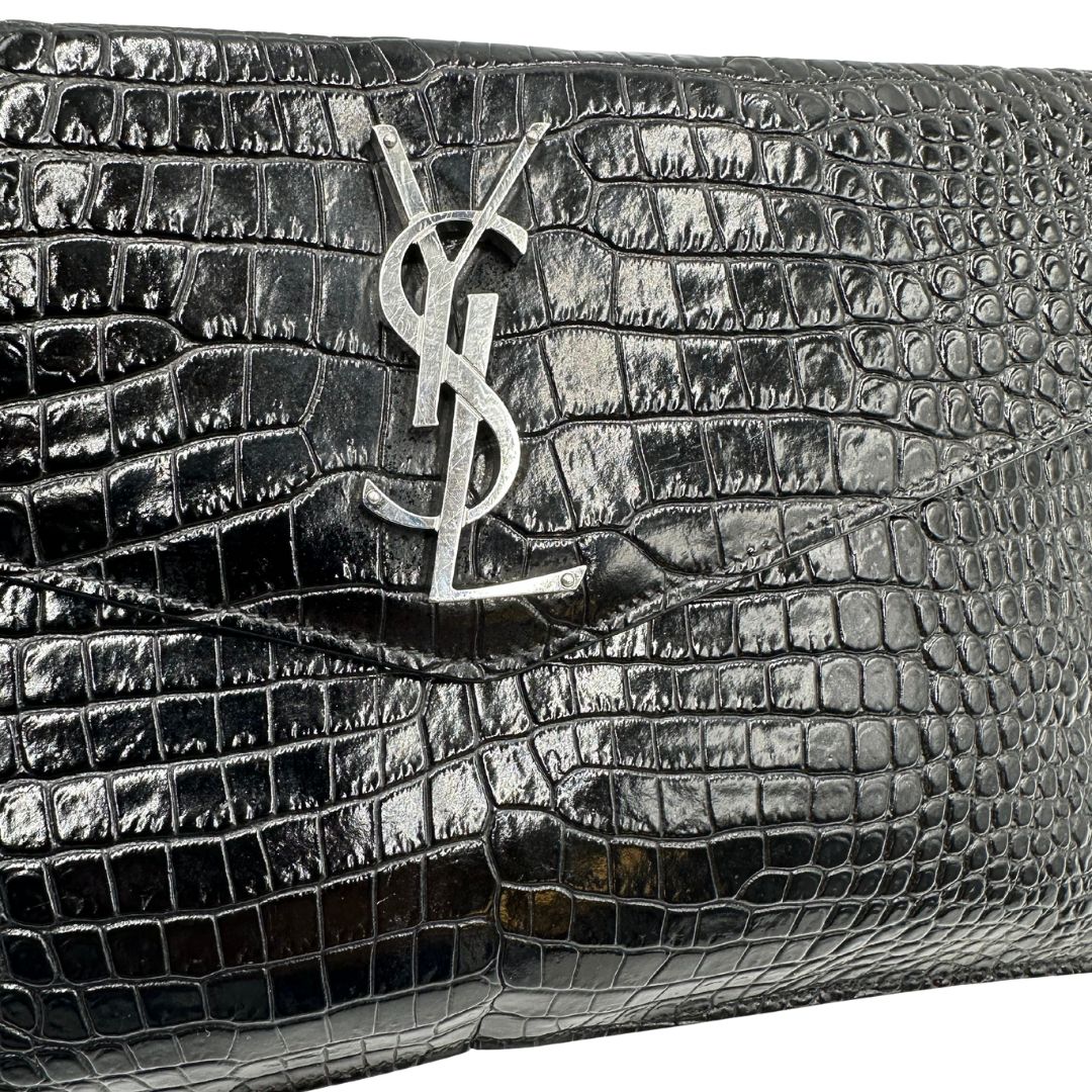 Logo di una pochette Saint Laurent in pelle nera lucida effetto cocco, impreziosita dal logo Cassandre sul front in metallo argentato. Munita di dustbag.