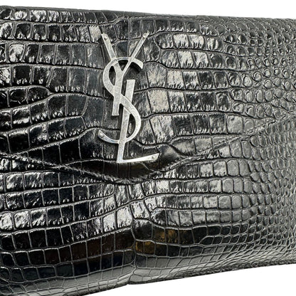 Logo di una pochette Saint Laurent in pelle nera lucida effetto cocco, impreziosita dal logo Cassandre sul front in metallo argentato. Munita di dustbag.