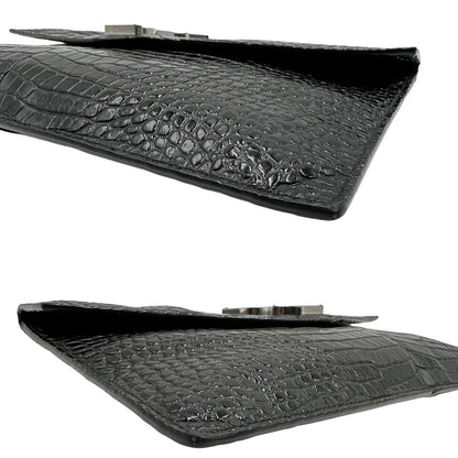 Angoli di una pochette Saint Laurent in pelle nera lucida effetto cocco, impreziosita dal logo Cassandre sul front in metallo argentato. Munita di dustbag.