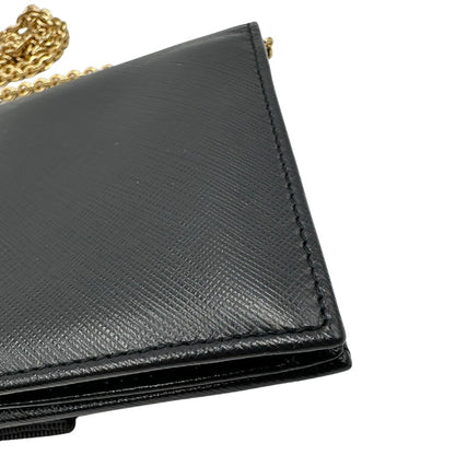Angolo di un WOC Salvatore Ferragamo in pelle saffiano nera con parti metalliche oro. Munita di una tracolla in catena amovibile e non regolabile. Chiusura con fiocco. Completo di dustbag. Indossabile a tracolla.