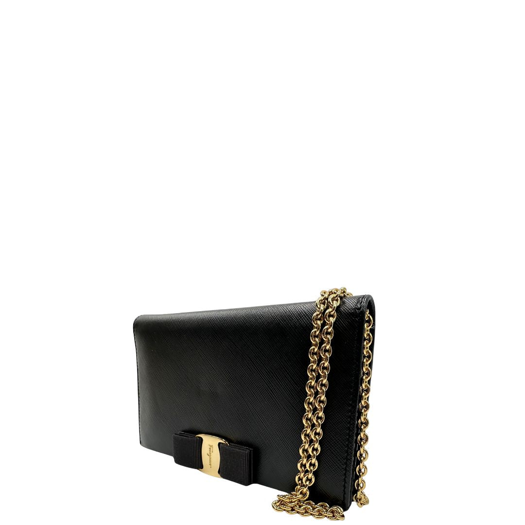 Laterale destro di un WOC Salvatore Ferragamo in pelle saffiano nera con parti metalliche oro. Munita di una tracolla in catena amovibile e non regolabile. Chiusura con fiocco. Completo di dustbag. Indossabile a tracolla.