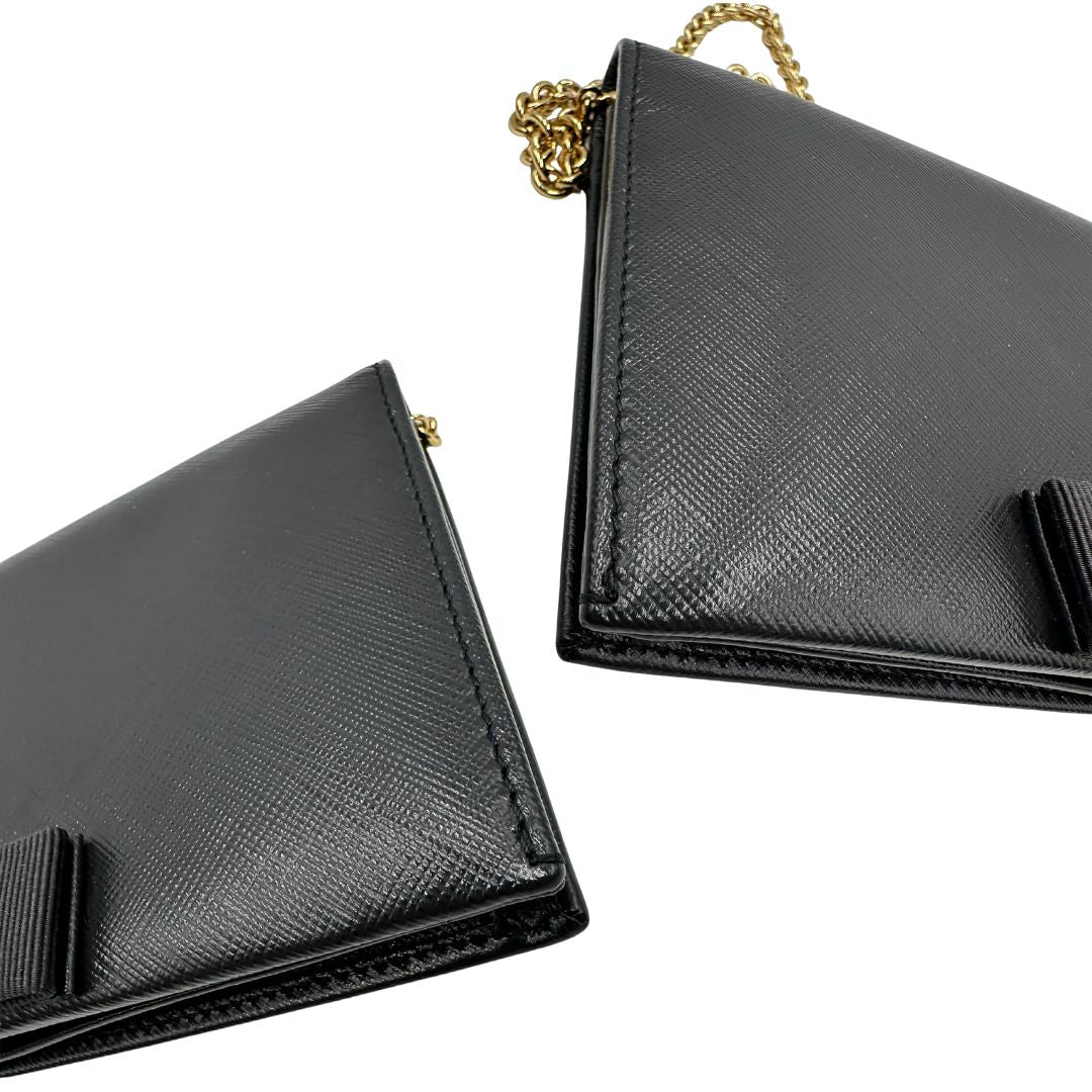 Angoli di un WOC Salvatore Ferragamo in pelle saffiano nera con parti metalliche oro. Munita di una tracolla in catena amovibile e non regolabile. Chiusura con fiocco. Completo di dustbag. Indossabile a tracolla.