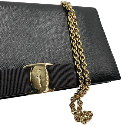 Fiocco della chiusura di un WOC Salvatore Ferragamo in pelle saffiano nera con parti metalliche oro. Munita di una tracolla in catena amovibile e non regolabile. Chiusura con fiocco. Completo di dustbag. Indossabile a tracolla.