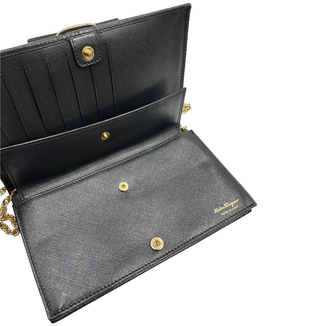 Apertura di un WOC Salvatore Ferragamo in pelle saffiano nera con parti metalliche oro. Munita di una tracolla in catena amovibile e non regolabile. Chiusura con fiocco. Completo di dustbag. Indossabile a tracolla.