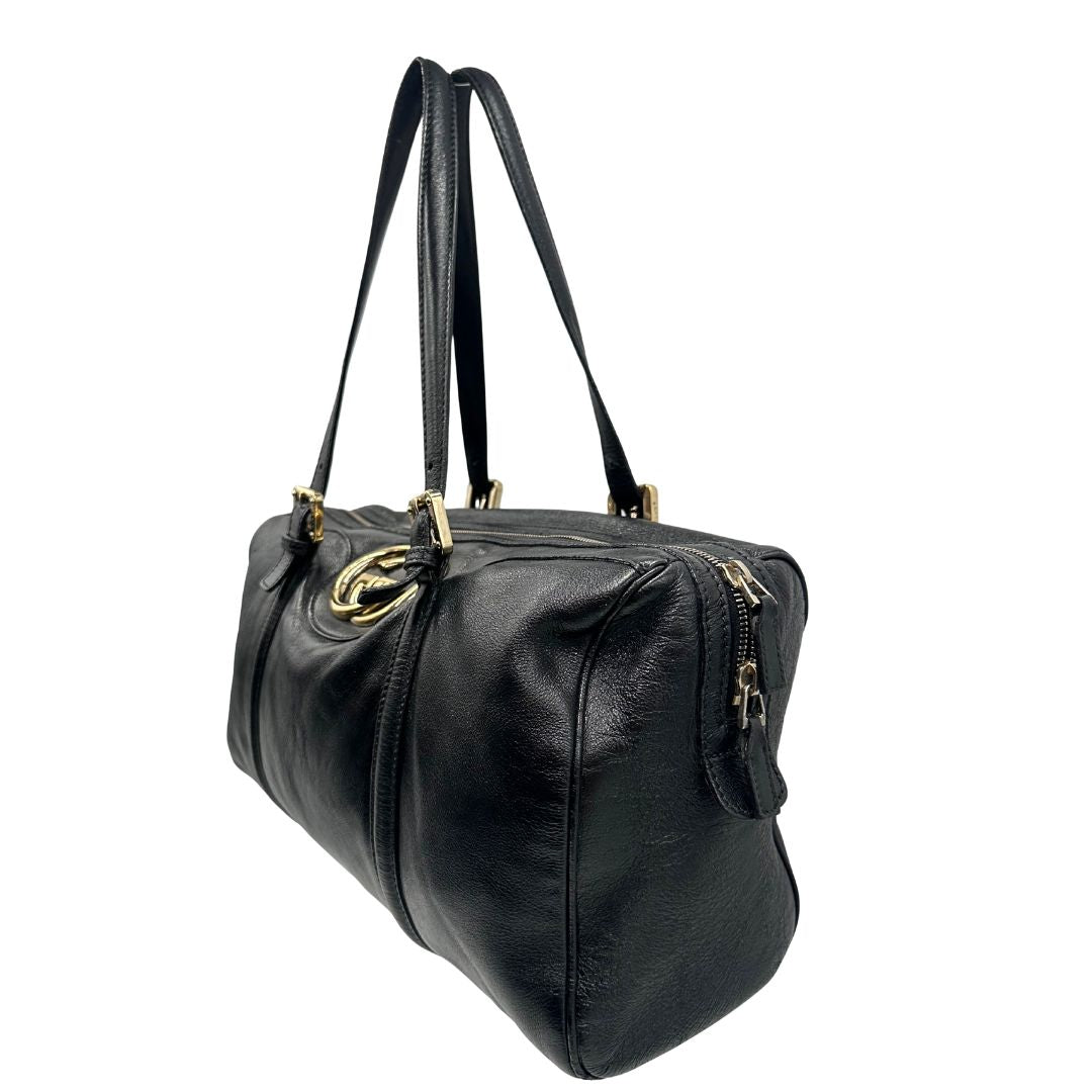 Lato sinistro di un Bauletto Gucci Britt Boston in pelle nera con parti metalliche dorate e doppi manici; da indossare a spalla. Rifinita con doppie G incrociate in metallo sul front. Completa di dustbag. Originale, usato, di lusso, in ottime condizioni.