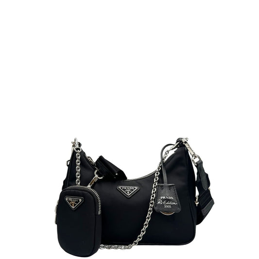 Front di una borsa Prada in nylon nero con parti metalliche argentate e finiture in pelle tono su tono; munita di una mini pouch amovibile, un accessorio portachiavi, manico in catena e una tracolla in tessuto amovibile e regolabile.