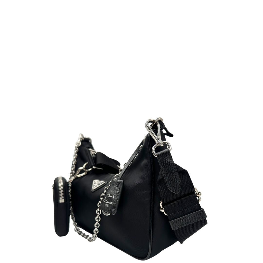 Laterale destro di una borsa Prada in nylon nero con parti metalliche argentate e finiture in pelle tono su tono; munita di una mini pouch amovibile, un accessorio portachiavi, manico in catena e una tracolla in tessuto amovibile e regolabile.