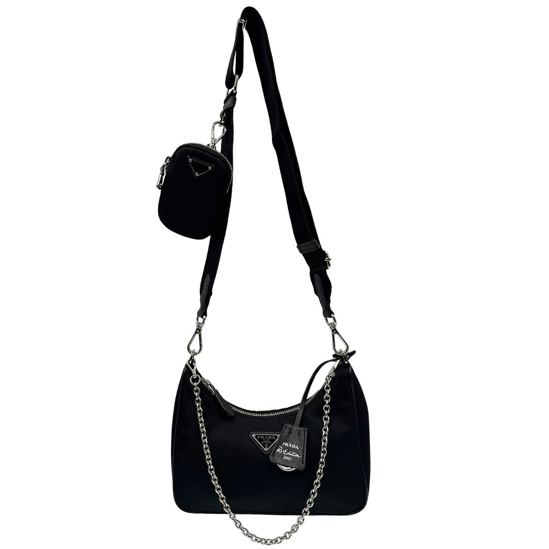Front di una borsa Prada in nylon nero con parti metalliche argentate e finiture in pelle tono su tono; munita di una mini pouch amovibile, un accessorio portachiavi, manico in catena e una tracolla in tessuto amovibile e regolabile.