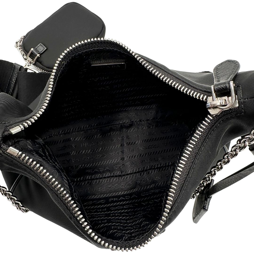 Interno di una borsa Prada in nylon nero con parti metalliche argentate e finiture in pelle tono su tono; munita di una mini pouch amovibile, un accessorio portachiavi, manico in catena e una tracolla in tessuto amovibile e regolabile.