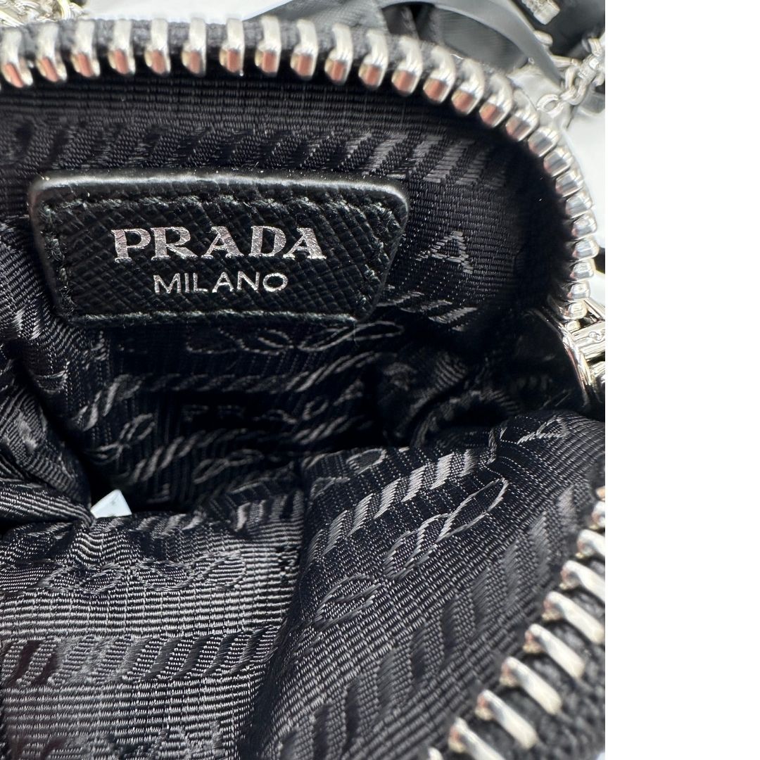 Interno della pouch di una borsa Prada in nylon nero con parti metalliche argentate e finiture in pelle tono su tono; munita di una mini pouch amovibile, un accessorio portachiavi, manico in catena e una tracolla in tessuto amovibile e regolabile.