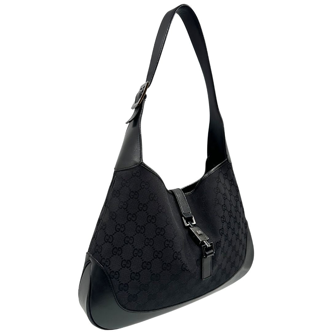 Laterale sinistro di una borsa Gucci in tessuto nero GG con finiture in pelle tono su tono e parti metalliche argentate. Munita di un manico leggermente regolabile.