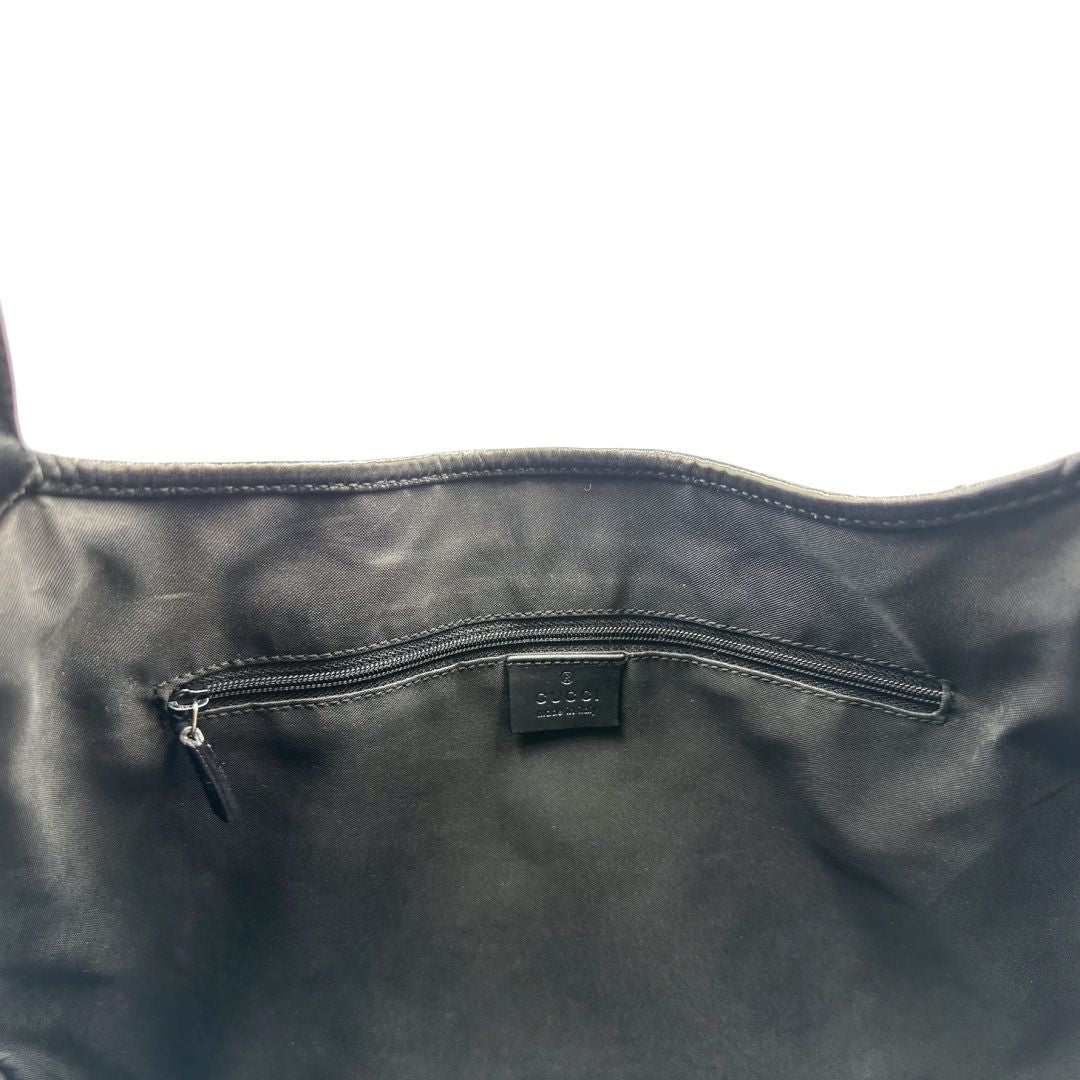 Interno di una borsa Gucci in tessuto nero GG con finiture in pelle tono su tono e parti metalliche argentate. Munita di un manico leggermente regolabile.