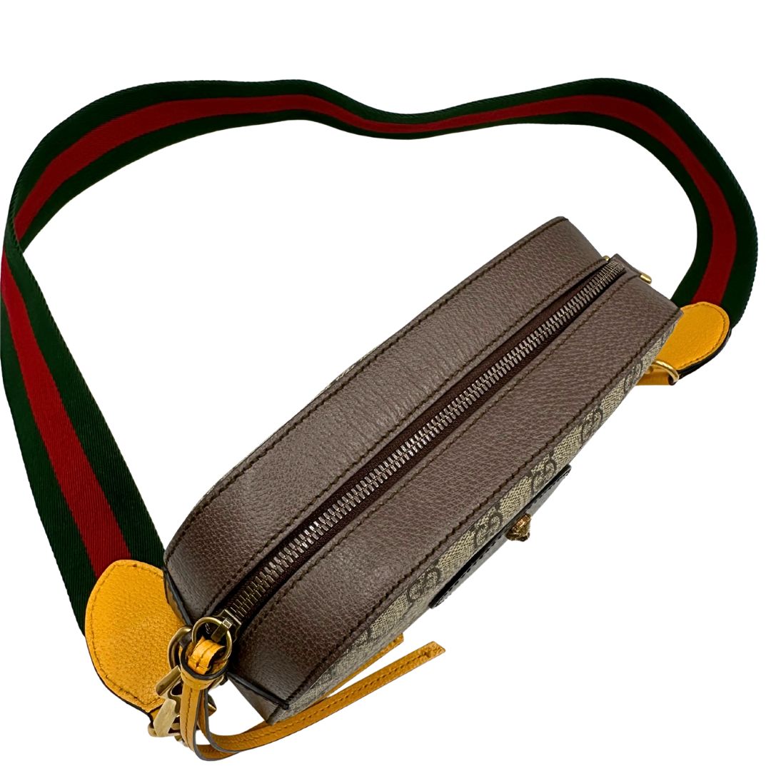 Chiusura di una borsa Gucci Neo Vintage in canvas beige GG Supreme con finiture in pelle marrone e parti metalliche dorate. Munita di una tracolla in tessuto Web verde e rosso, con dettagli in pelle gialla. Rifinita con logo lettering sul front e testa di tigre decorativa. Completa di dustbag.