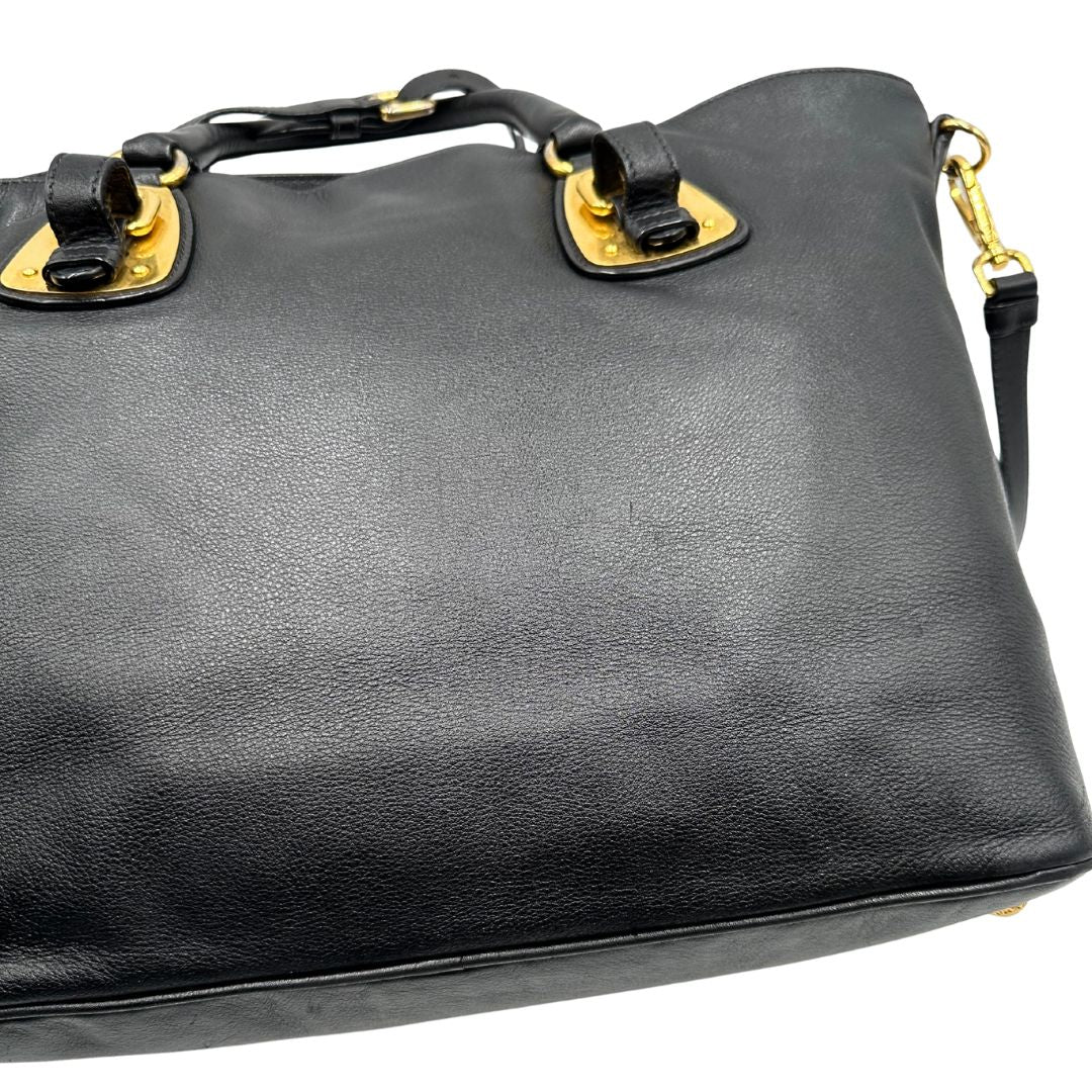 Difetti del pellame di una borsa Prada in pelle nera con parti metalliche dorate; munita di una tracolla amovibile e regolabile e doppi manici stondati.