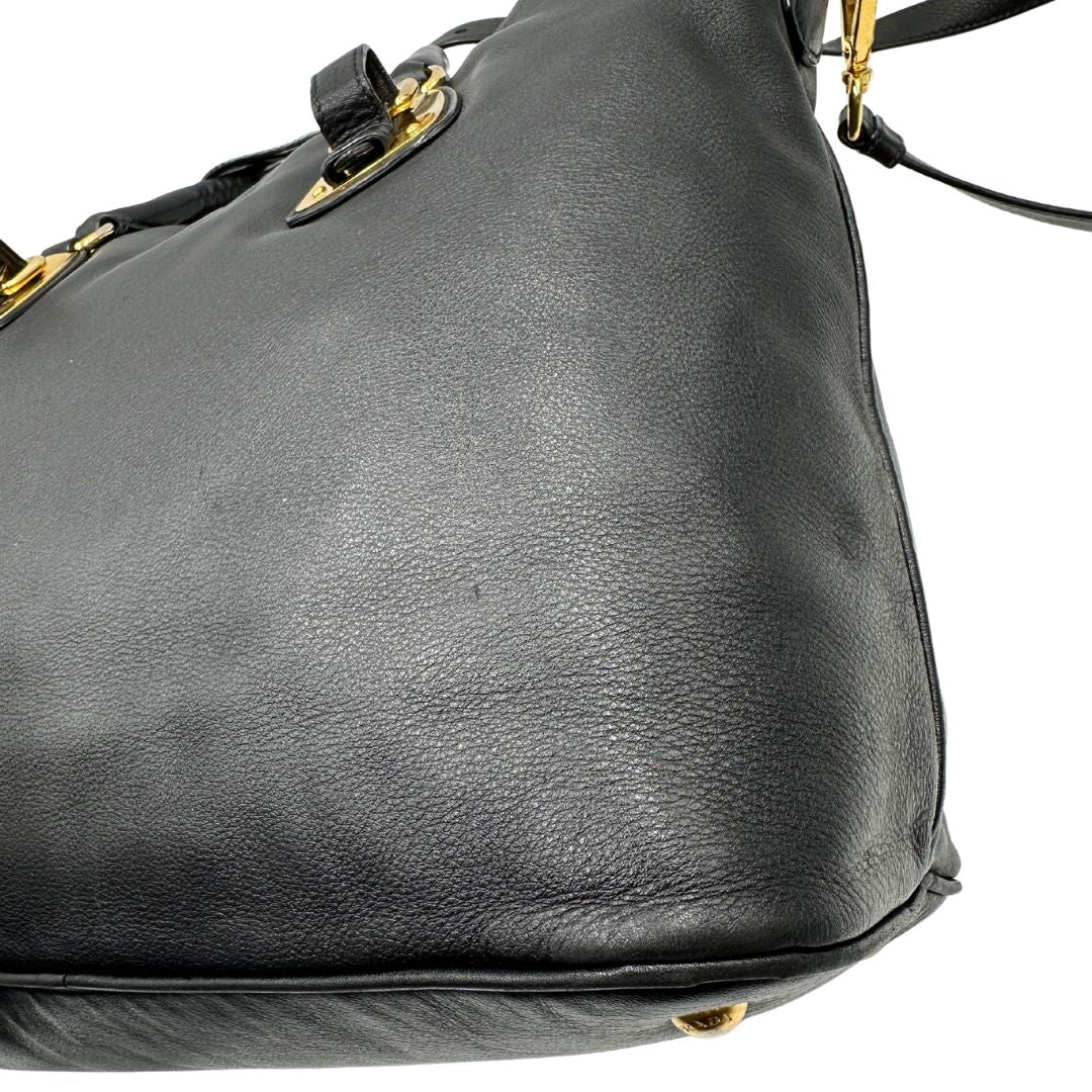 Difetto del pellame di una borsa Prada in pelle nera con parti metalliche dorate; munita di una tracolla amovibile e regolabile e doppi manici stondati.