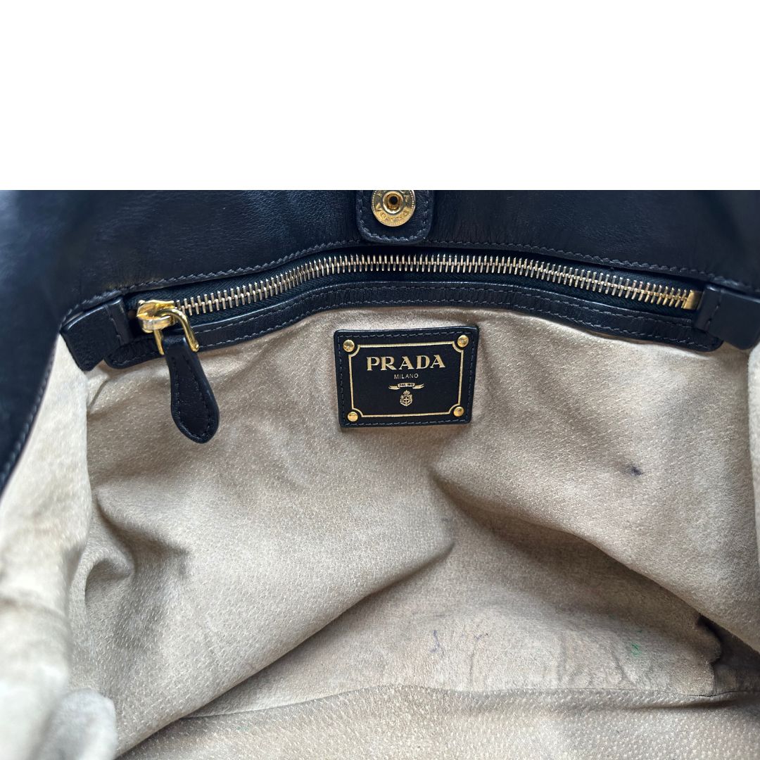Interno di una borsa Prada in pelle nera con parti metalliche dorate; munita di una tracolla amovibile e regolabile e doppi manici stondati.