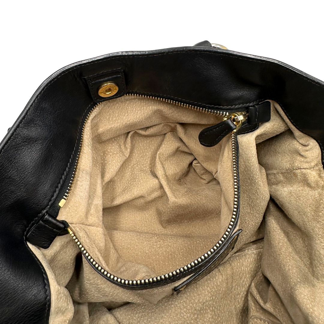 Interno di una borsa Prada in pelle nera con parti metalliche dorate; munita di una tracolla amovibile e regolabile e doppi manici stondati.