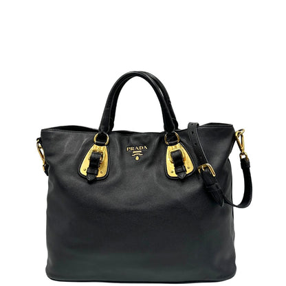 Front di una borsa Prada in pelle nera con parti metalliche dorate; munita di una tracolla amovibile e regolabile e doppi manici stondati.