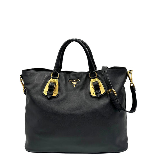Front di una borsa Prada in pelle nera con parti metalliche dorate; munita di una tracolla amovibile e regolabile e doppi manici stondati.