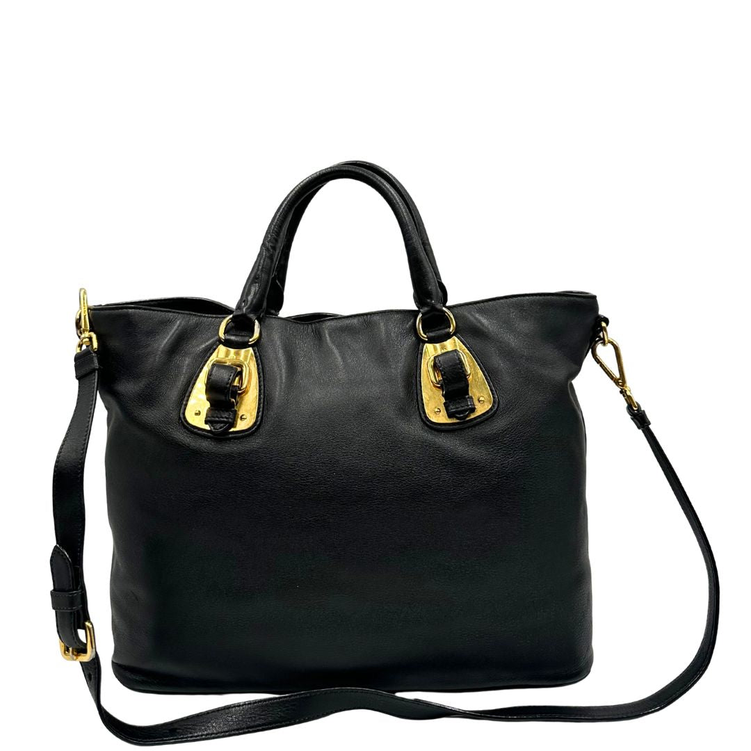 Retro di una borsa Prada in pelle nera con parti metalliche dorate; munita di una tracolla amovibile e regolabile e doppi manici stondati.
