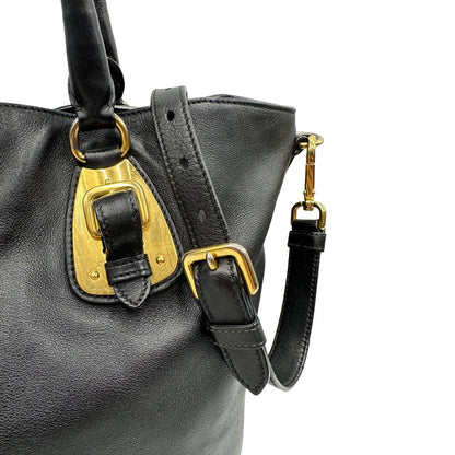 Fibbie di una borsa Prada in pelle nera con parti metalliche dorate; munita di una tracolla amovibile e regolabile e doppi manici stondati.