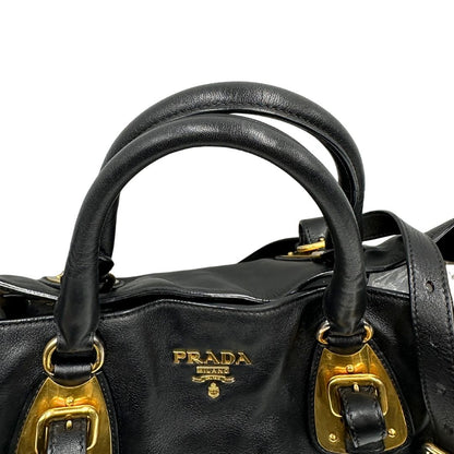 Manici di una borsa Prada in pelle nera con parti metalliche dorate; munita di una tracolla amovibile e regolabile e doppi manici stondati.