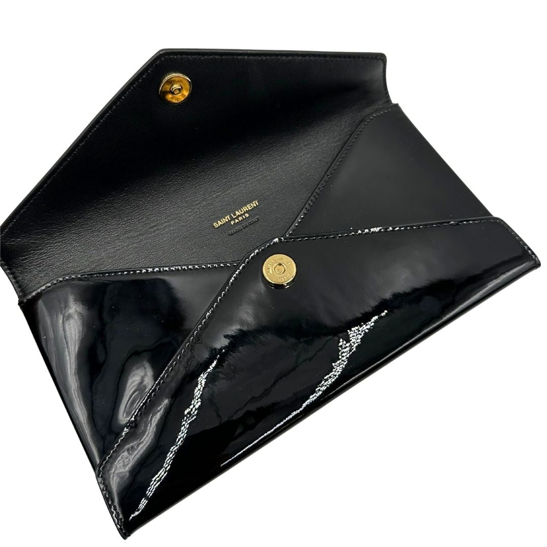 Apertura di una pochette Paloma Envelope Saint Laurent in vernice nera lucida con chiusura a bottone a pressione e parti metalliche dorate. Interno in pelle con logo impresso. Completa di scatola e sacchetto antipolvere.