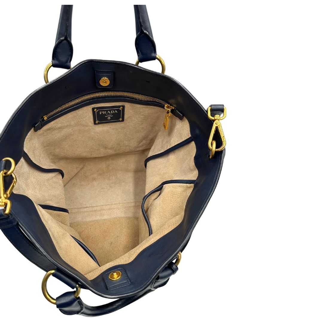 Interno di una Borsa Prada in pelle blu notte con parti metalliche dorate; munita di un accessorio porta address, doppi manici stondati e una tracolla amovibile e regolabile. Indossabile a mano oppure a tracolla. Originale, usata, di lusso, in ottime condizioni.