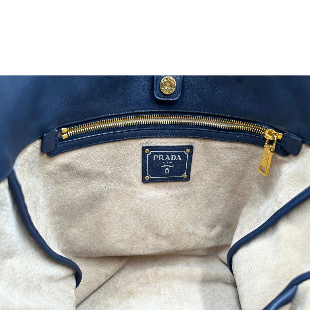 Interno di una Borsa Prada in pelle blu notte con parti metalliche dorate; munita di un accessorio porta address, doppi manici stondati e una tracolla amovibile e regolabile. Indossabile a mano oppure a tracolla. Originale, usata, di lusso, in ottime condizioni.