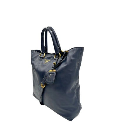 Lato sinistro di una Borsa Prada in pelle blu notte con parti metalliche dorate; munita di un accessorio porta address, doppi manici stondati e una tracolla amovibile e regolabile. Indossabile a mano oppure a tracolla. Originale, usata, di lusso, in ottime condizioni.