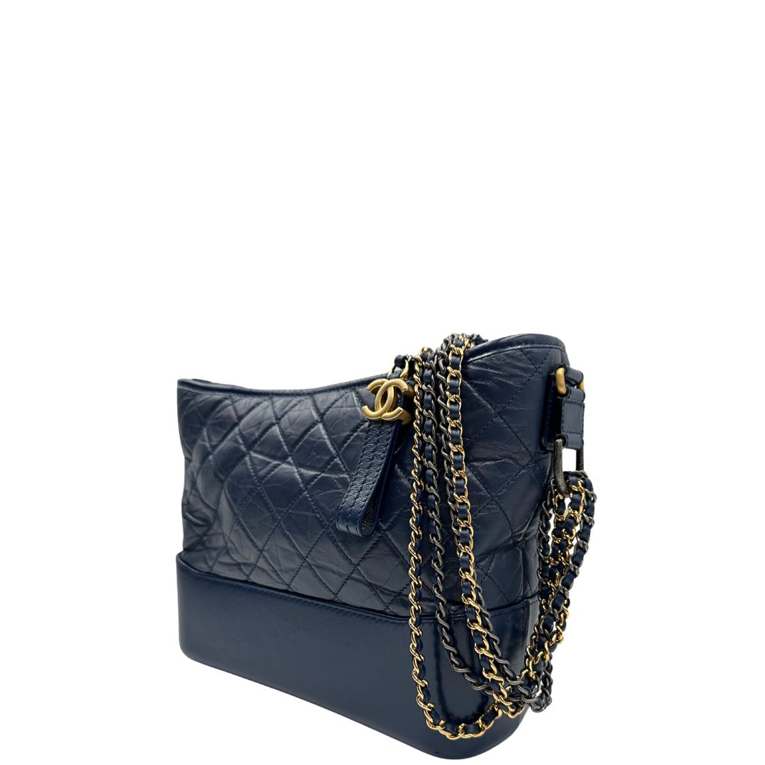 Laterale destro di una borsa Chanel Gabrielle in pelle matelassé blu navy con parti metalliche dorate e argentate. Munita di una tracolla in catena e pelle intrecciata con spallaccio. Tirante delle cerniera impreziosito dall'iconico logo CC in metallo dorato, completa di corredo.