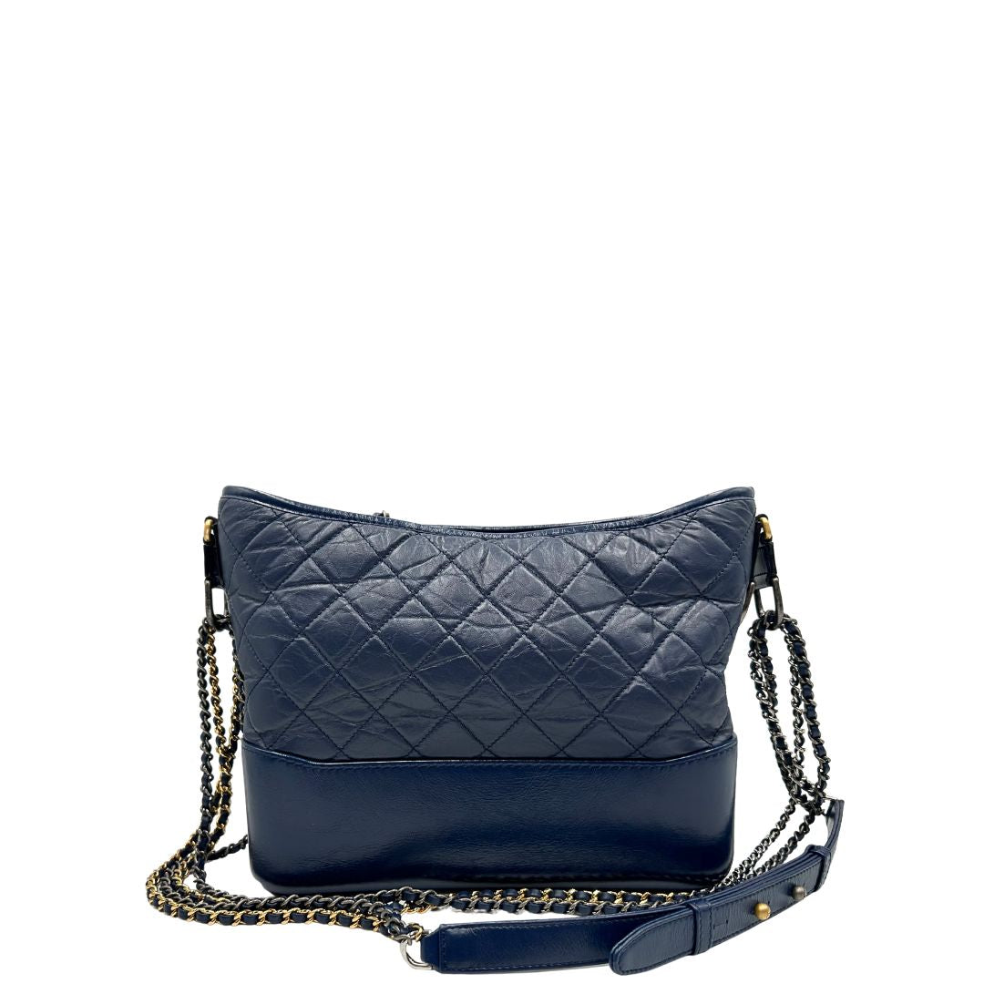 Retro di una borsa Chanel Gabrielle in pelle matelassé blu navy con parti metalliche dorate e argentate. Munita di una tracolla in catena e pelle intrecciata con spallaccio. Tirante delle cerniera impreziosito dall'iconico logo CC in metallo dorato, completa di corredo.