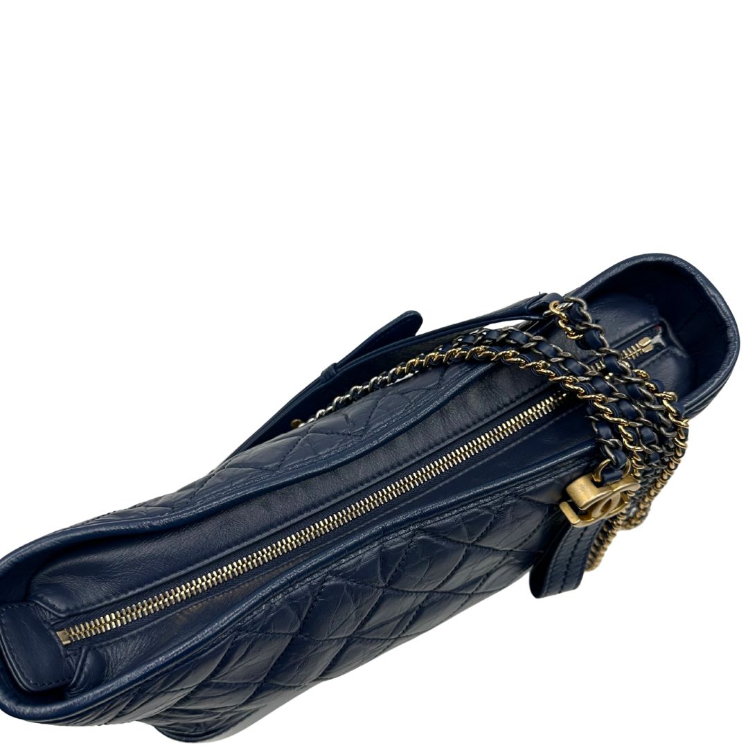 Vista superiore della chiusura di una borsa Chanel Gabrielle in pelle matelassé blu navy con parti metalliche dorate e argentate. Munita di una tracolla in catena e pelle intrecciata con spallaccio. Tirante delle cerniera impreziosito dall'iconico logo CC in metallo dorato, completa di corredo.