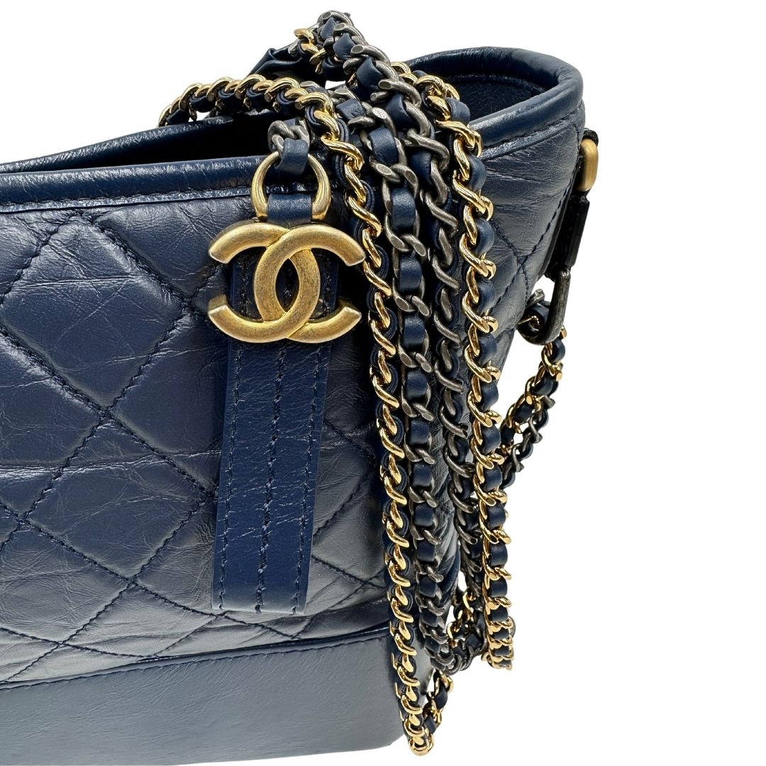 Parti metalliche di una borsa Chanel Gabrielle in pelle matelassé blu navy con parti metalliche dorate e argentate. Munita di una tracolla in catena e pelle intrecciata con spallaccio. Tirante delle cerniera impreziosito dall'iconico logo CC in metallo dorato, completa di corredo.
