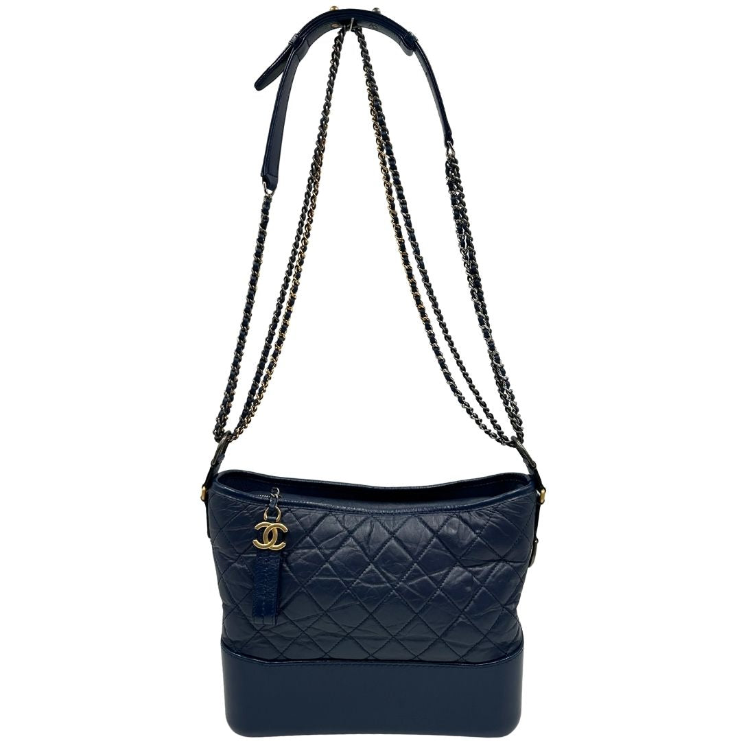 Front di una borsa Chanel Gabrielle in pelle matelassé blu navy con parti metalliche dorate e argentate. Munita di una tracolla in catena e pelle intrecciata con spallaccio. Tirante delle cerniera impreziosito dall'iconico logo CC in metallo dorato, completa di corredo.