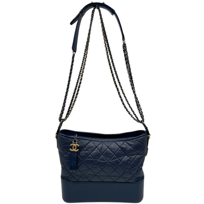 Front di una borsa Chanel Gabrielle in pelle matelassé blu navy con parti metalliche dorate e argentate. Munita di una tracolla in catena e pelle intrecciata con spallaccio. Tirante delle cerniera impreziosito dall'iconico logo CC in metallo dorato, completa di corredo.