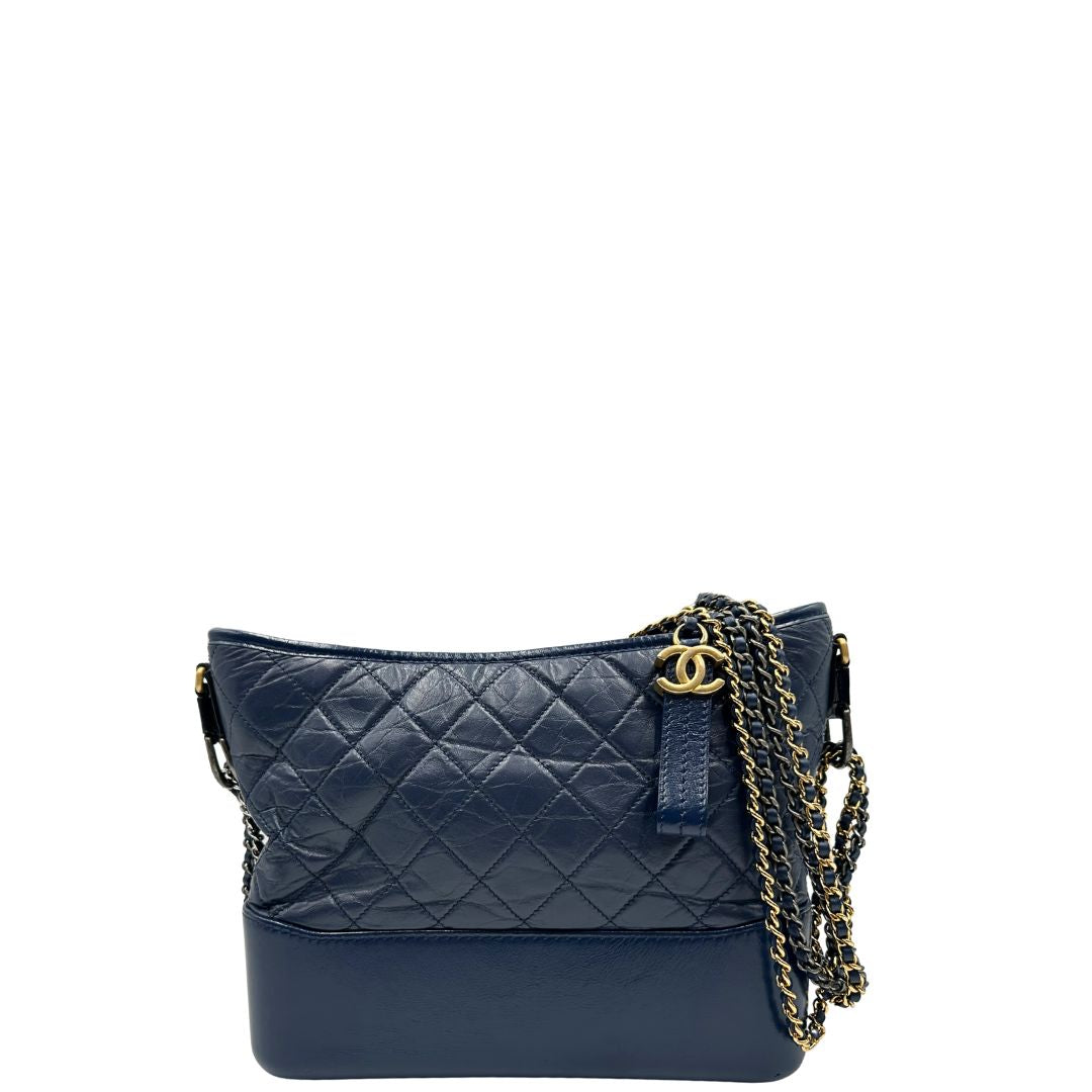 Front di una borsa Chanel Gabrielle in pelle matelassé blu navy con parti metalliche dorate e argentate. Munita di una tracolla in catena e pelle intrecciata con spallaccio. Tirante delle cerniera impreziosito dall'iconico logo CC in metallo dorato, completa di corredo.