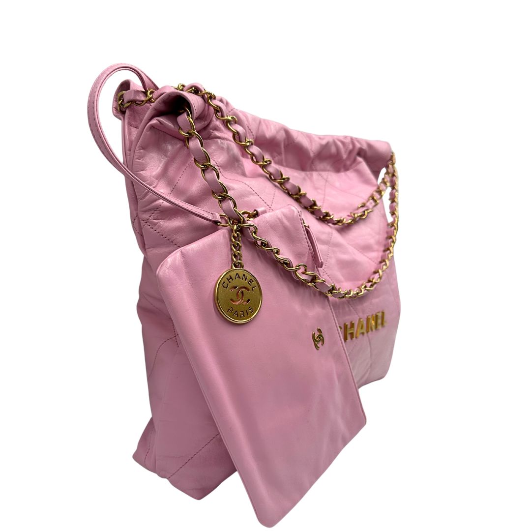 Laterale sinistro di una borsa Chanel 22 in pelle trapuntata rosa con parti metalliche dorate; dotata di pochette estraibile e amovibile, doppi manici in catena e pelle per portarla a spalla. Chiusura con bottone automatici. Completa di scatola e dustbag.