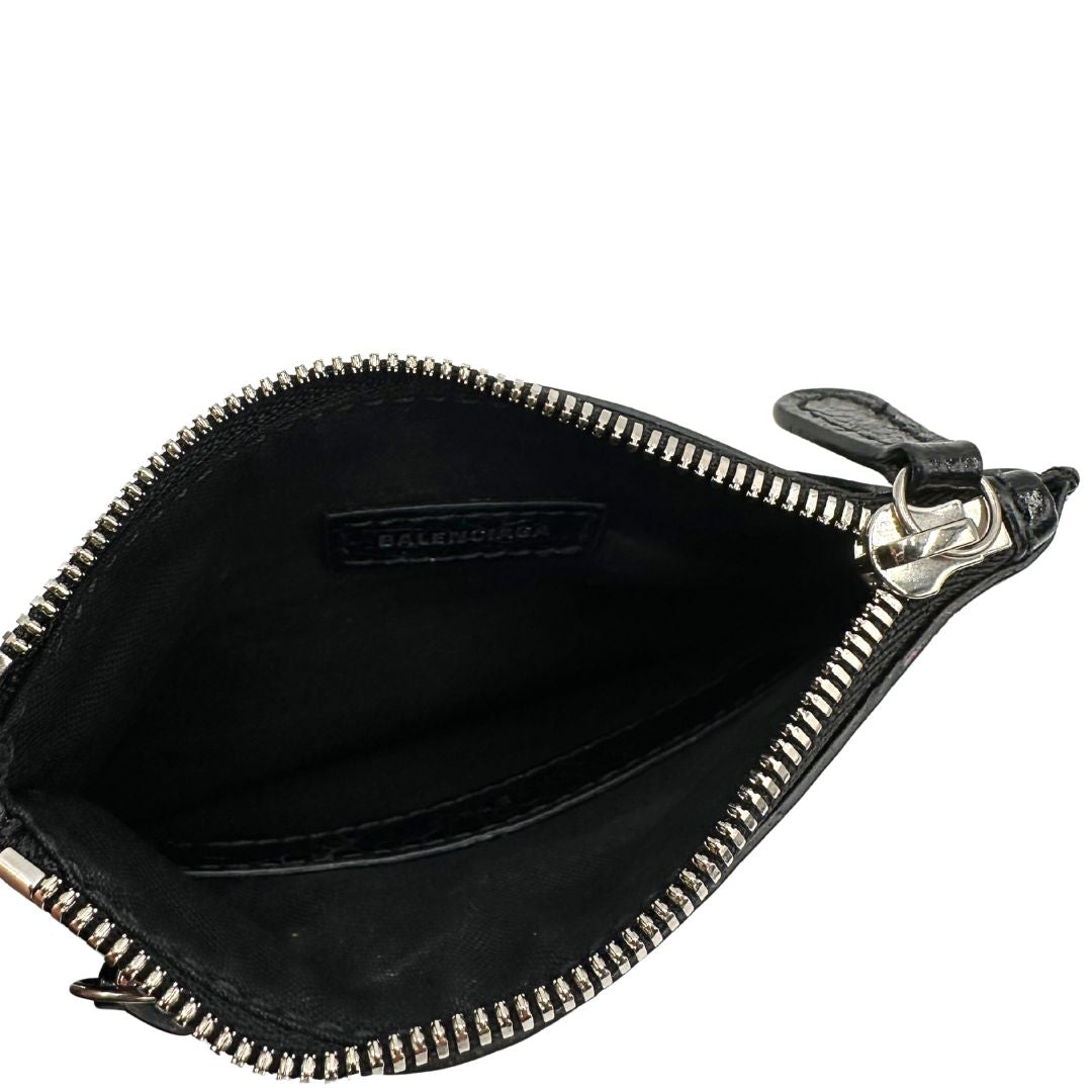 Interno di una pochette Balenciaga in pelle effetto invecchiato nera, con parti metalliche argentate; munita di uno specchietto a forma di cuore, polsino amovibile e un mini porta monete e carte. Completa di dustbag.