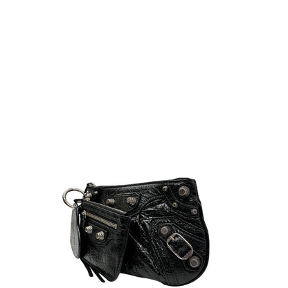 Laterale destro di una pochette Balenciaga in pelle effetto invecchiato nera, con parti metalliche argentate; munita di uno specchietto a forma di cuore, polsino amovibile e un mini porta monete e carte. Completa di dustbag.