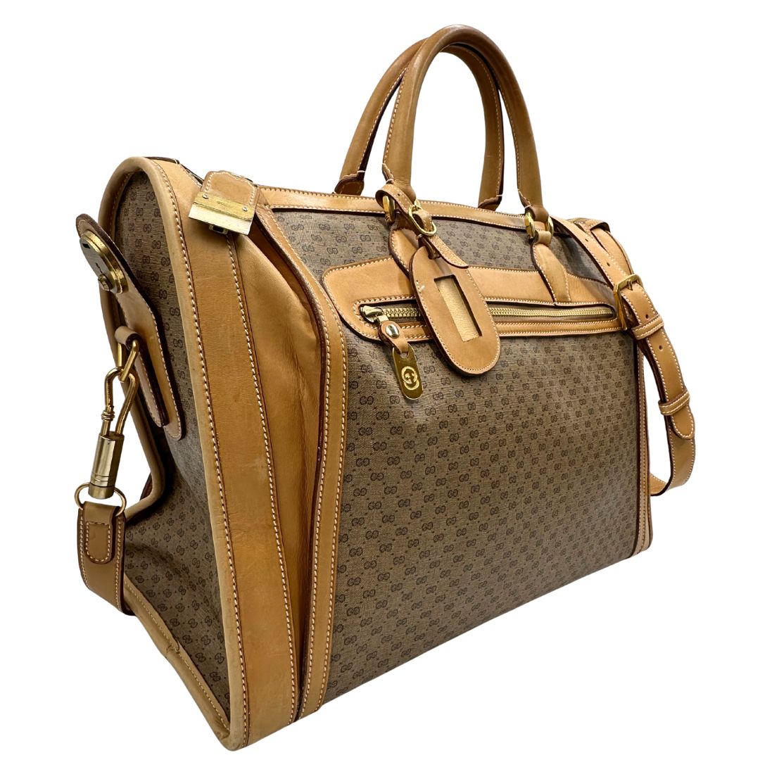 Laterale sinistro di una borsa Gucci in canvas beige GG con finiture in pelle color cammello e parti metalliche dorate, munita di doppi manici stondati e di una tracolla amovibile e regolabile. Dotata di tag porta address.