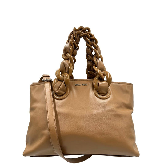 Front di una borsa Miu Miu in pelle color cammello con parti metalliche argentate; munita di doppi manici intrecciata in PVC e pelle e di una tracolla amovibile e regolabile. Completa di dustbag.