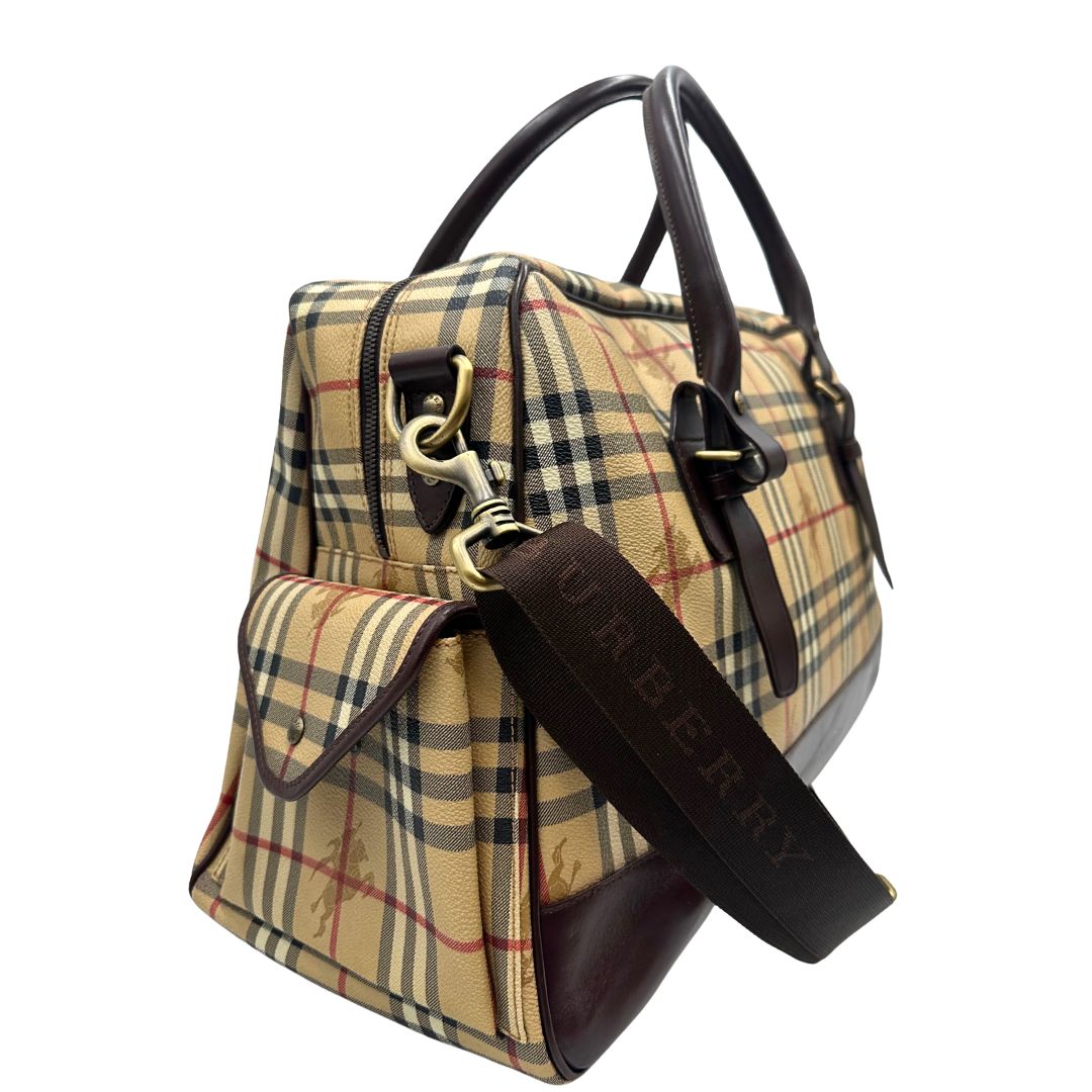 Laterale sinistro di un borsone Burberry in canvas trama tartan con finiture in pelle marrone testa di moro e parti metalliche dorate; munito di doppi manici stondati e una tracolla amovibile e regolabile.