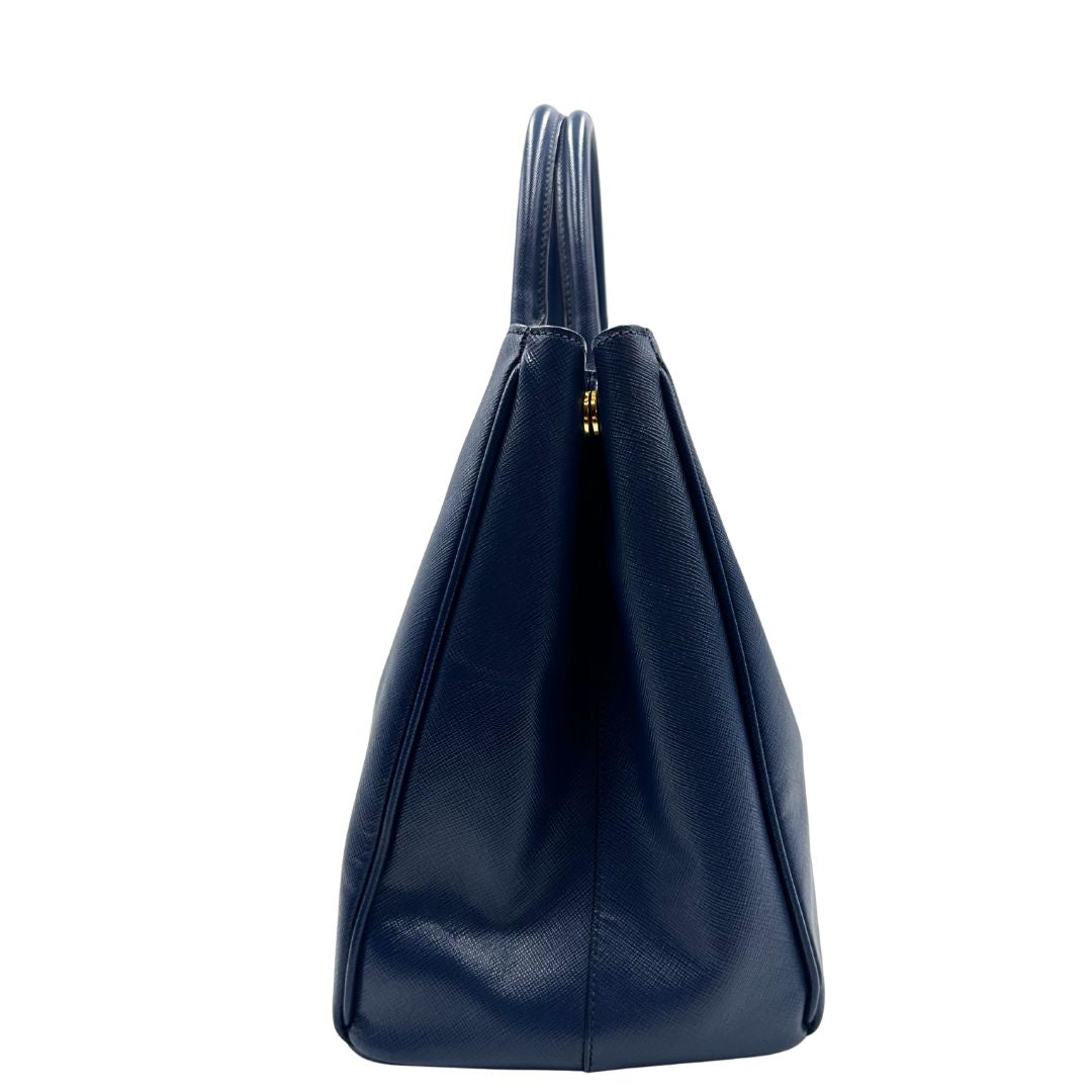 laterale della Borsa Prada in pelle saffiano blu con parti metalliche dorate; munita di doppi manici stondati e impreziosita da una clochette portachiavi, di lusso, originale, ottime condizioni, usata.