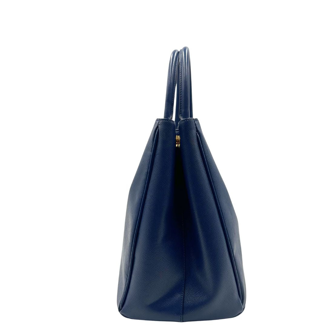 laterale della Borsa Prada in pelle saffiano blu con parti metalliche dorate; munita di doppi manici stondati e impreziosita da una clochette portachiavi, di lusso, originale, ottime condizioni, usata.