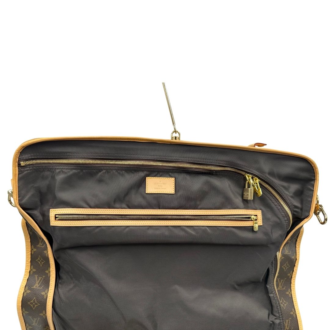 Borsa da viaggio porta abiti in canvas marrone monogram con finiture in vacchetta naturale e parti metalliche dorate; munita di un manico singolo, una tracolla amovibile e regolabile e 2 grucce. Completa di Lucchetti e una chiave, dustbag.