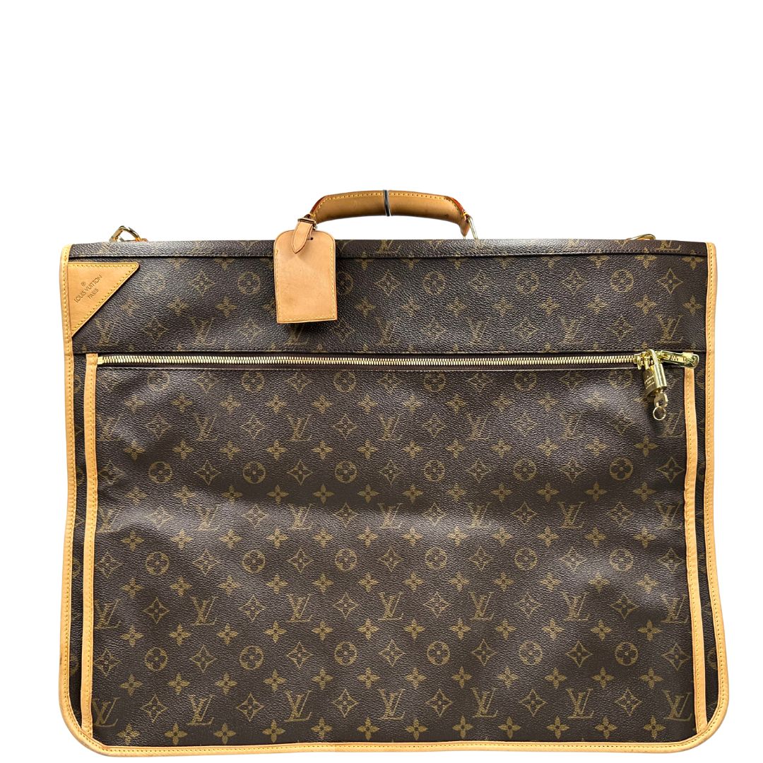 Front di una Borsa da viaggio porta abiti in canvas marrone monogram con finiture in vacchetta naturale e parti metalliche dorate; munita di un manico singolo, una tracolla amovibile e regolabile e 2 grucce. Completa di Lucchetti e una chiave, dustbag.