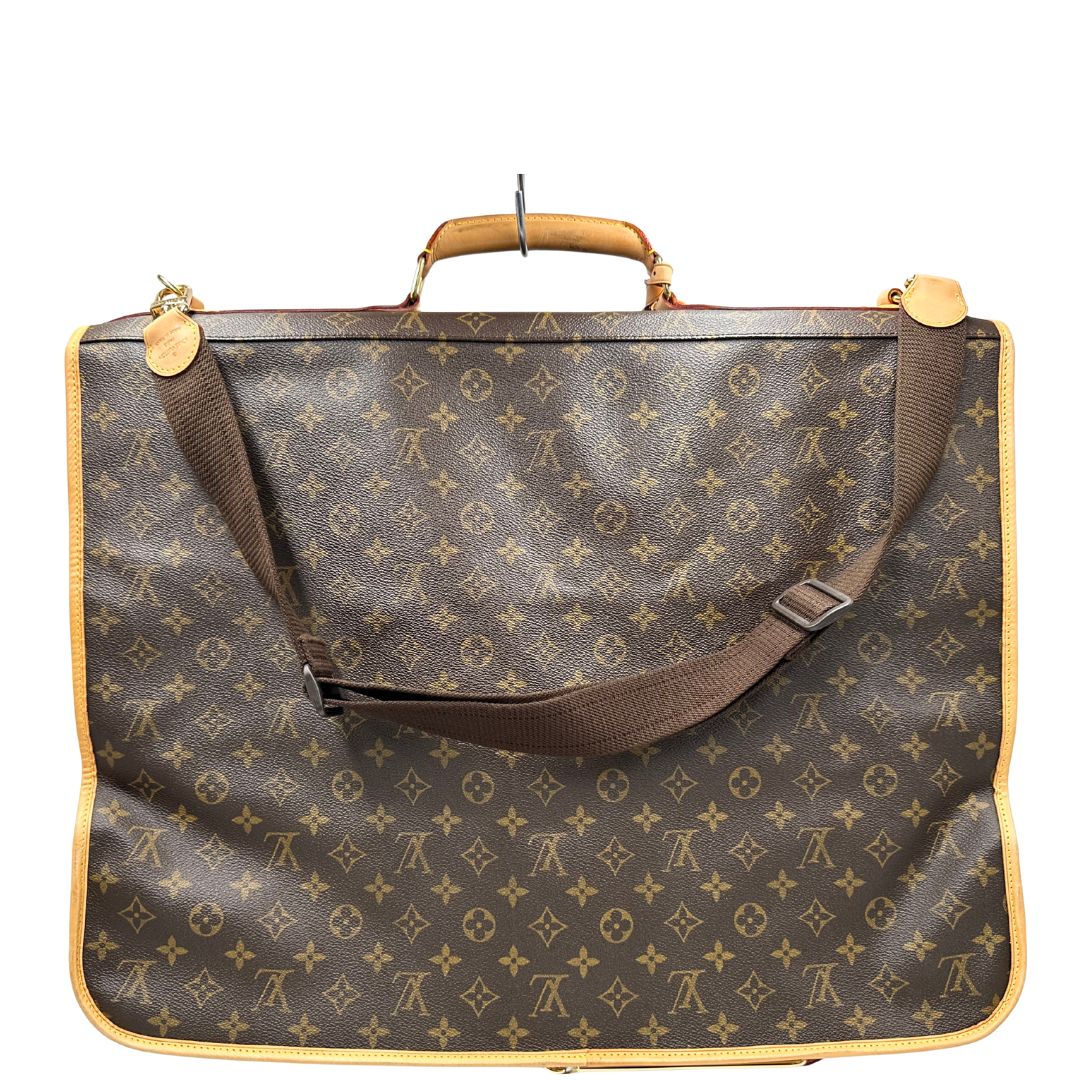 Retro una Borsa da viaggio porta abiti in canvas marrone monogram con finiture in vacchetta naturale e parti metalliche dorate; munita di un manico singolo, una tracolla amovibile e regolabile e 2 grucce. Completa di Lucchetti e una chiave, dustbag.