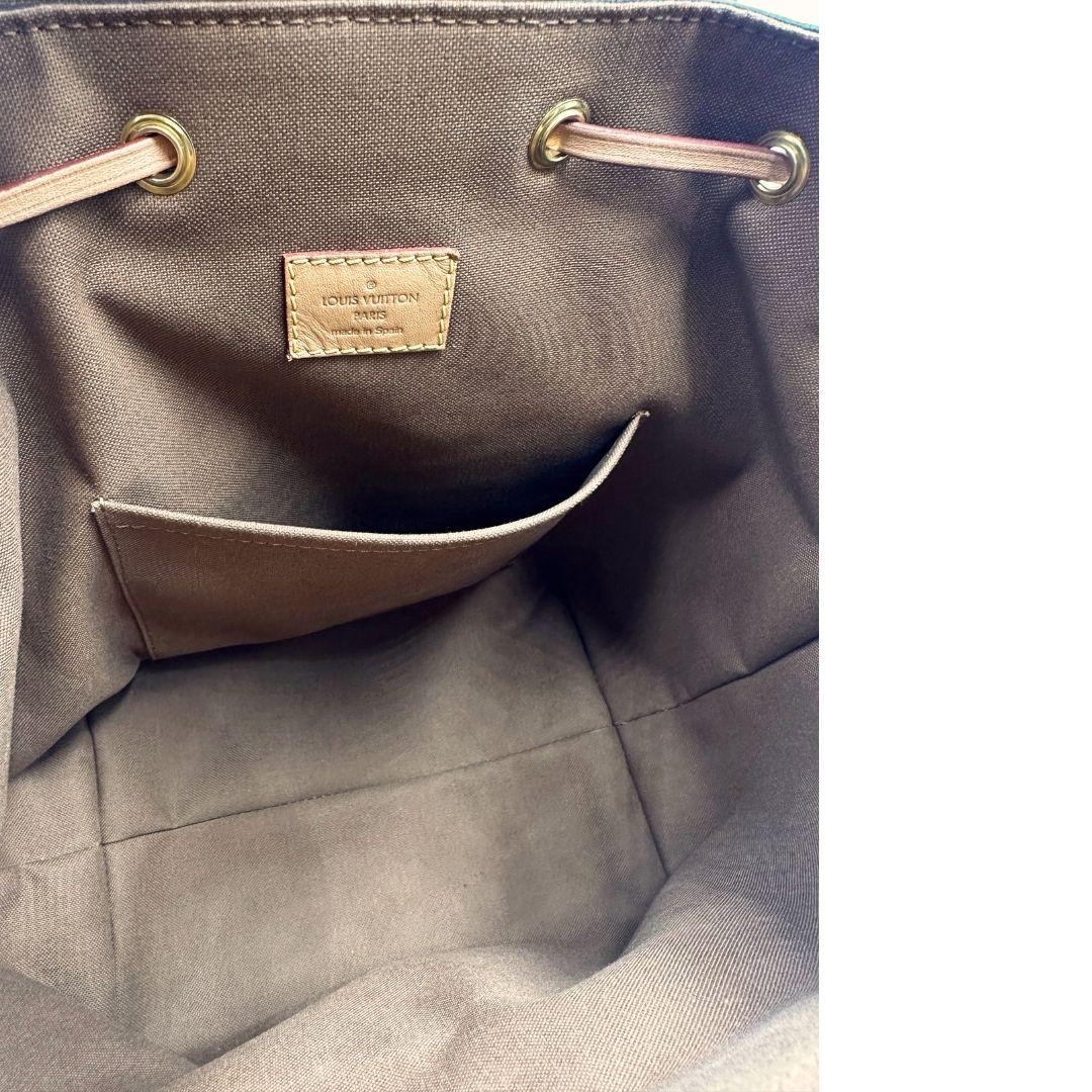 Interno di uno zaino Montsouris NM in canvas marrone monogram con finiture in vacchetta naturale e parti metalliche dorate, munito di un manico sulla parte superiore e due bretelle in vacchetta regolabili. Completo di corredo e charm decorativo.
