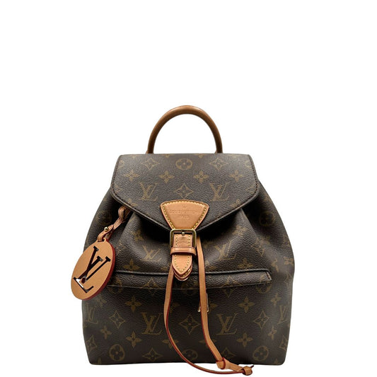 Front di uno zaino Montsouris NM in canvas marrone monogram con finiture in vacchetta naturale e parti metalliche dorate, munito di un manico sulla parte superiore e due bretelle in vacchetta regolabili. Completo di corredo e charm decorativo.